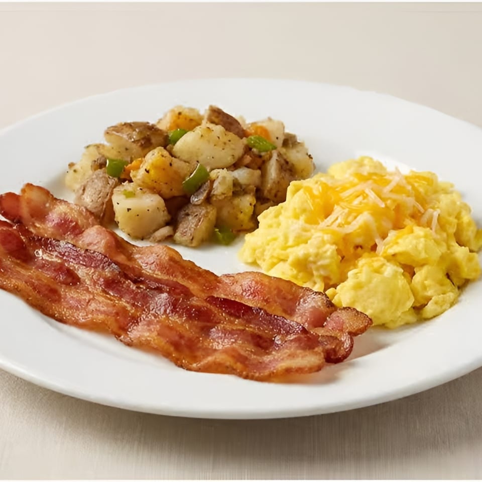 A breakfast plate with crispy bacon, cheesy scrambled eggs, and seasoned home fries.