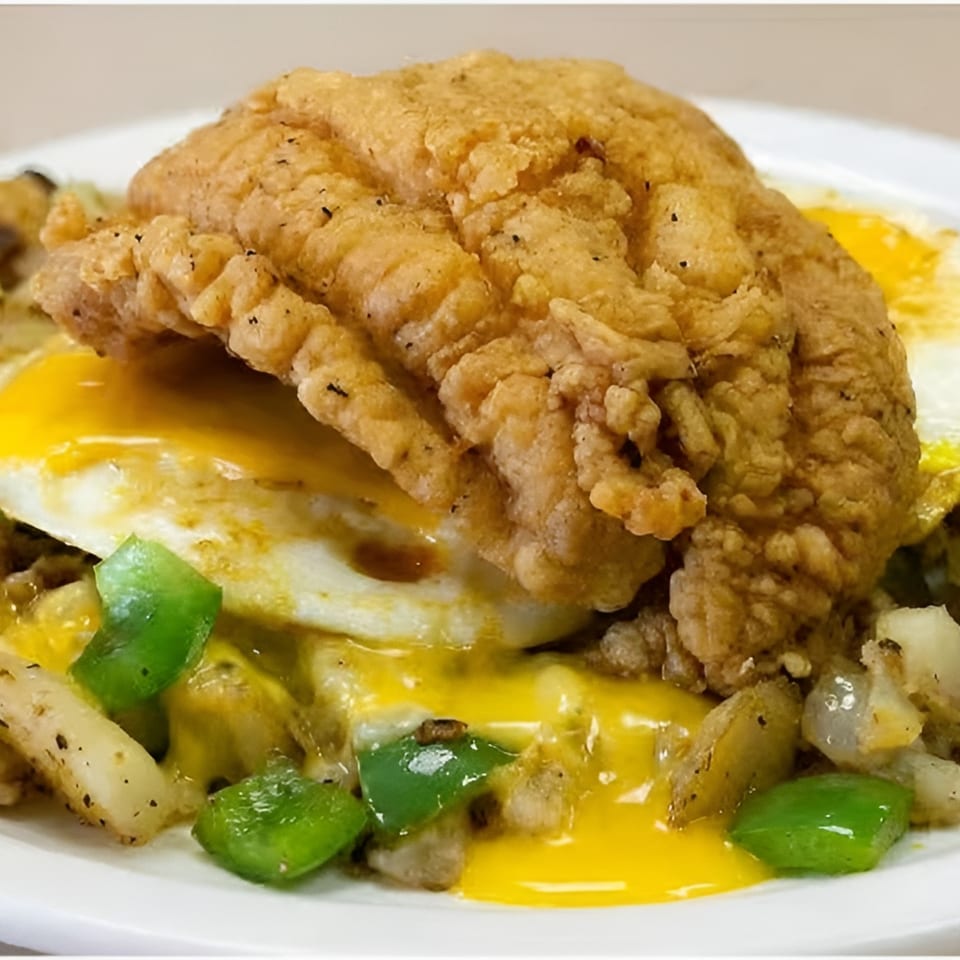 Crispy fried fish fillet over fried eggs, potatoes, green peppers, and melted cheese.